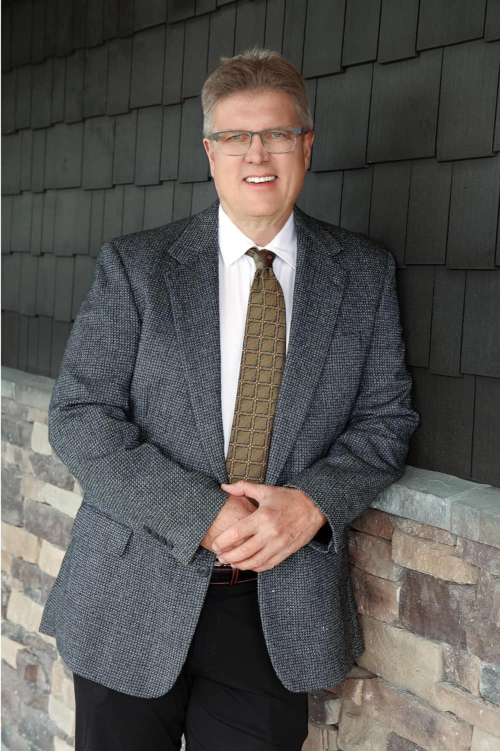 Man in business attire, smiling against wall.